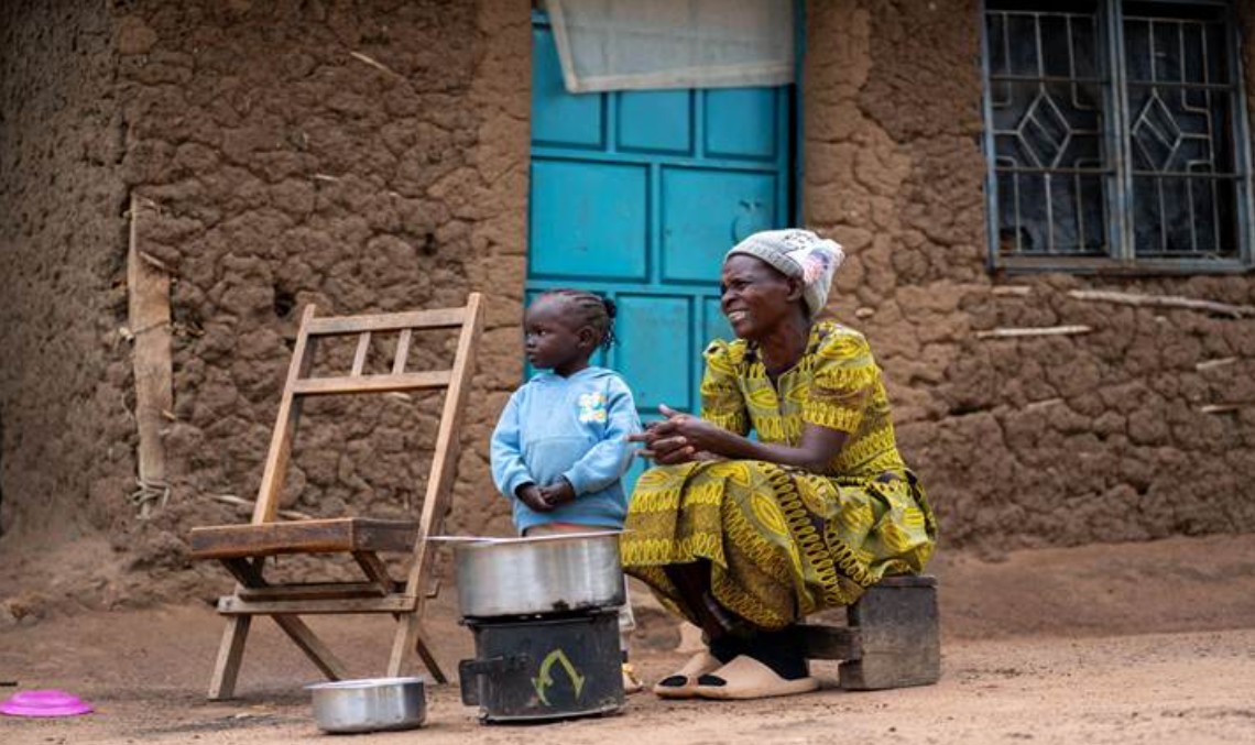 A woman, seated, and a young boy, standing, by a small stove in Kenya.